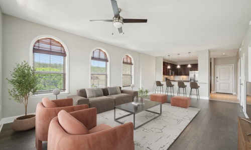 Modern open-plan living room with arched windows, sectional sofa, accent chairs, coffee table, and a kitchen island with bar stools in a bright contemporary apartment