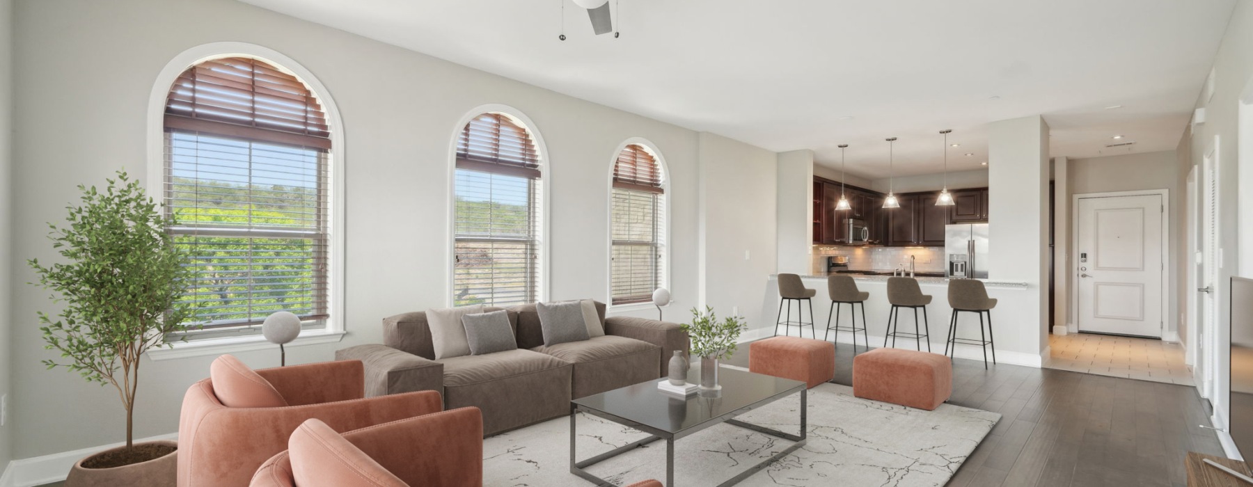 Modern open-plan living room with arched windows, sectional sofa, accent chairs, coffee table, and a kitchen island with bar stools in a bright contemporary apartment